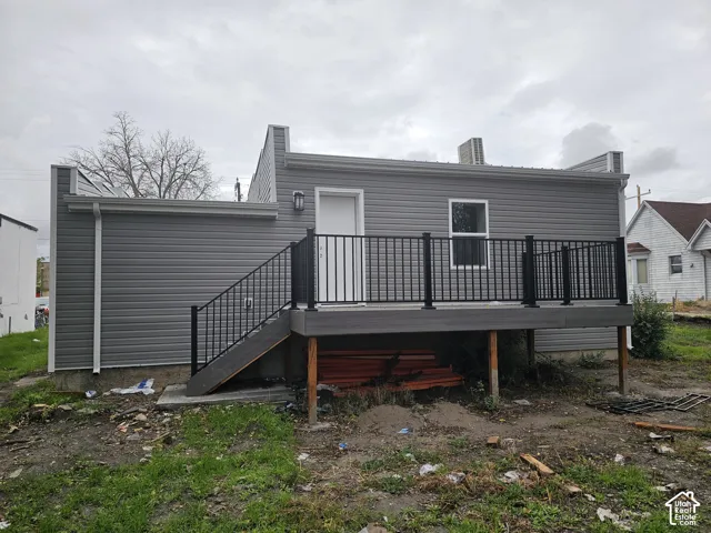 Exterior featuring gray siding, a deck with black metal railings, a white exterior door, a single window, and an outdoor wall-mounted light fixture
