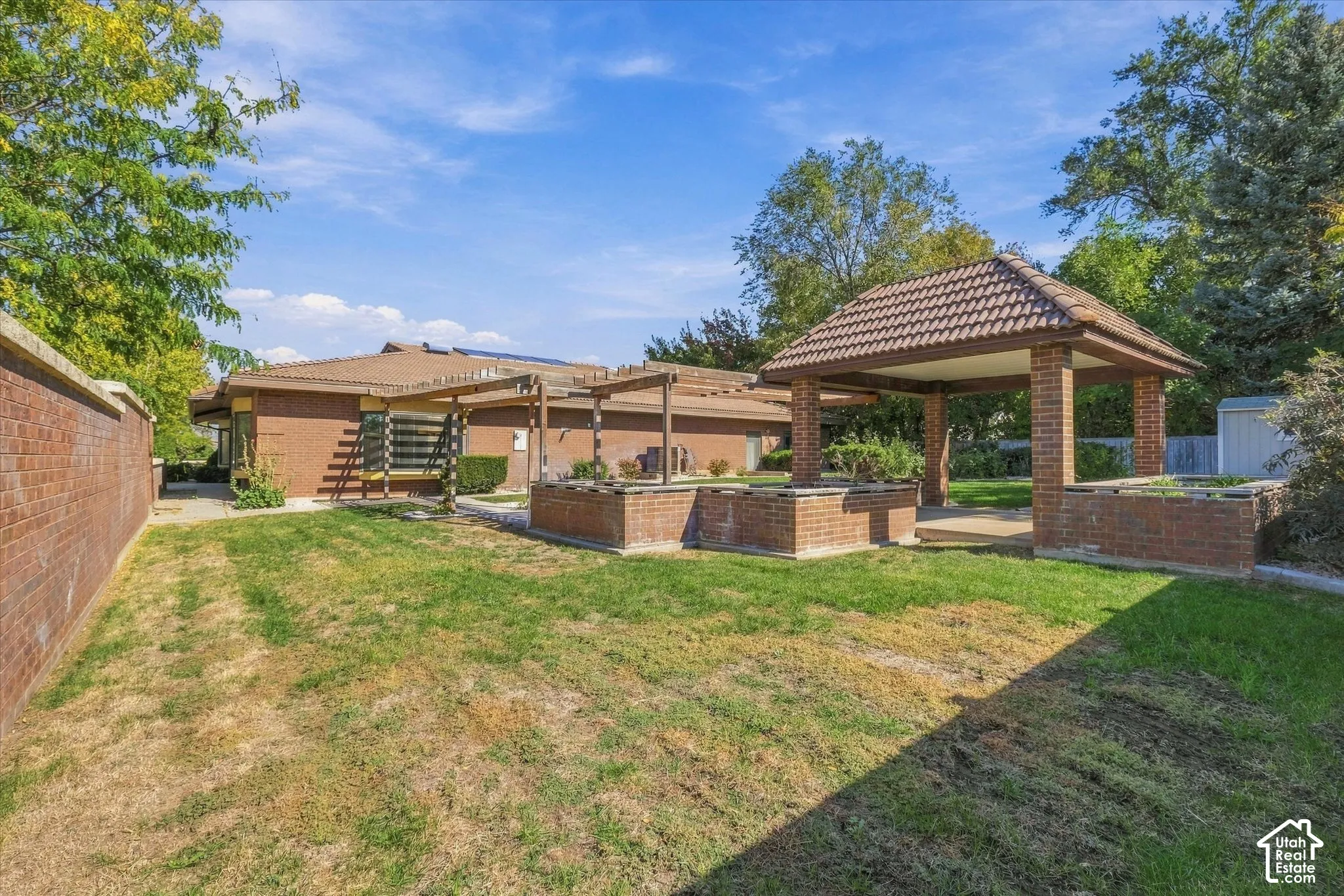 Expansive backyard featuring a brick gazebo with a tiled roof, brick planters, a brick privacy wall, and mature perimeter trees