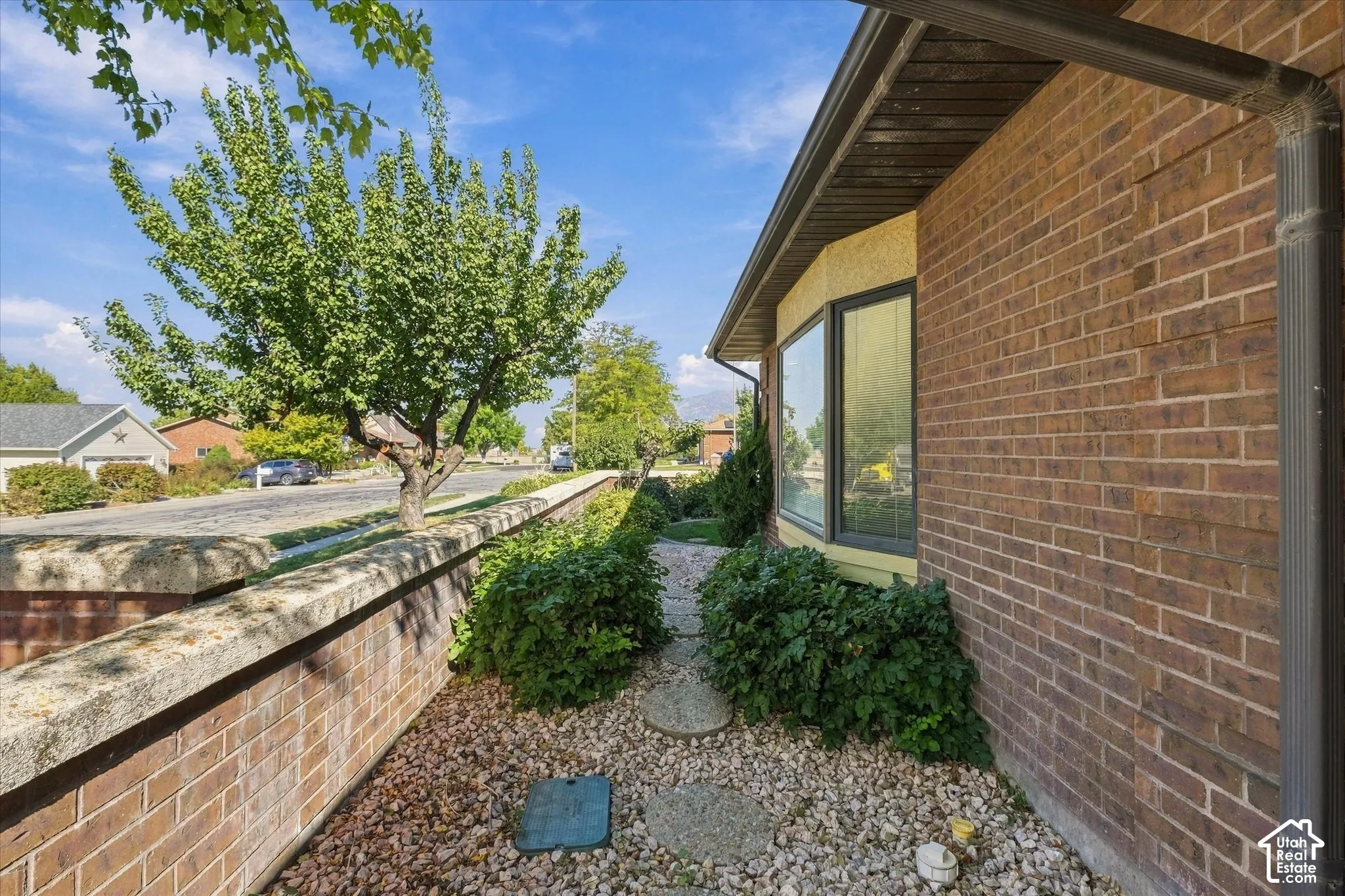 Brick exterior with a bay window, rain gutters, and a stone-lined pathway