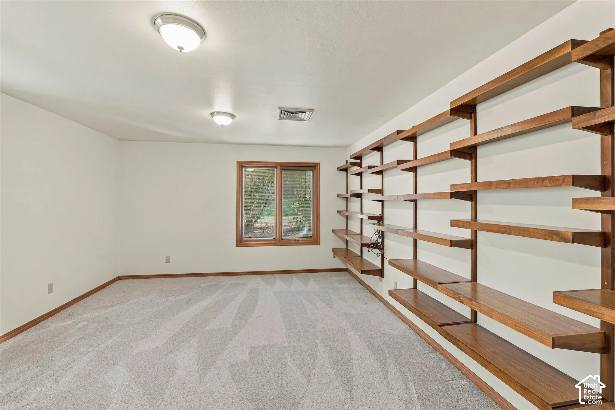 Carpeted room with a window, two flush-mount ceiling lights, and extensive built-in shelving