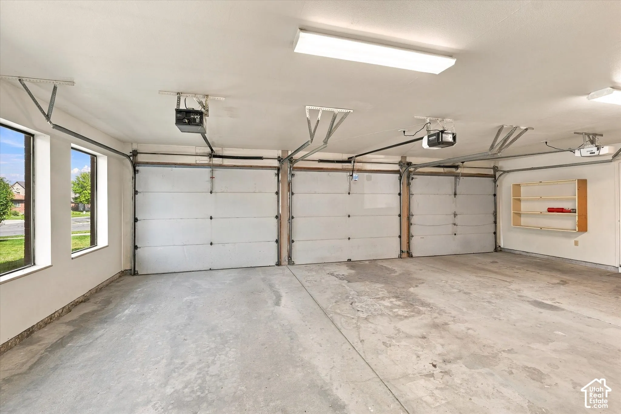 Three garage doors with automatic openers, concrete flooring, dual windows, and built-in shelving