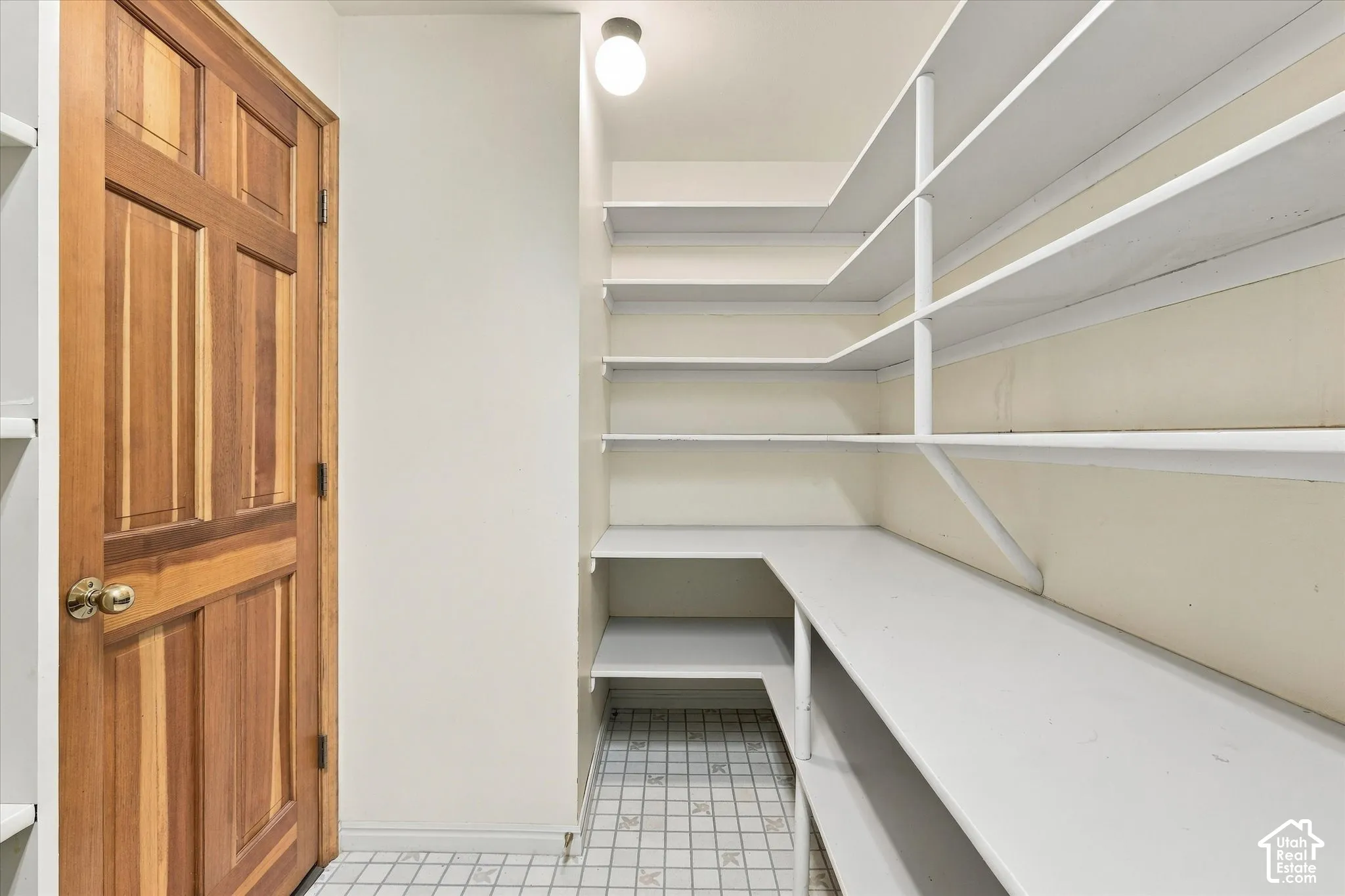 Large panty with extensive storage, wood-paneled door and tiled flooring.