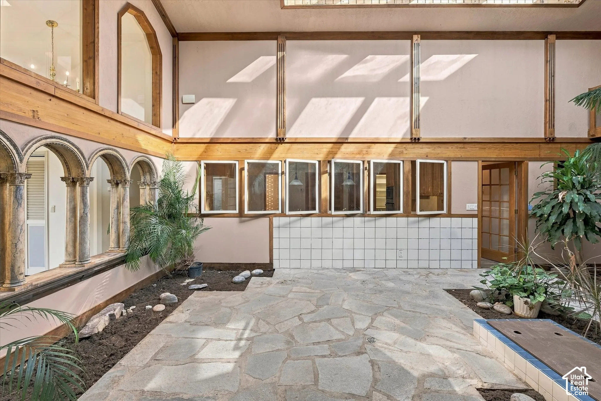 Stone tile flooring with exposed wood beams, arched doorways, and upper-level windows