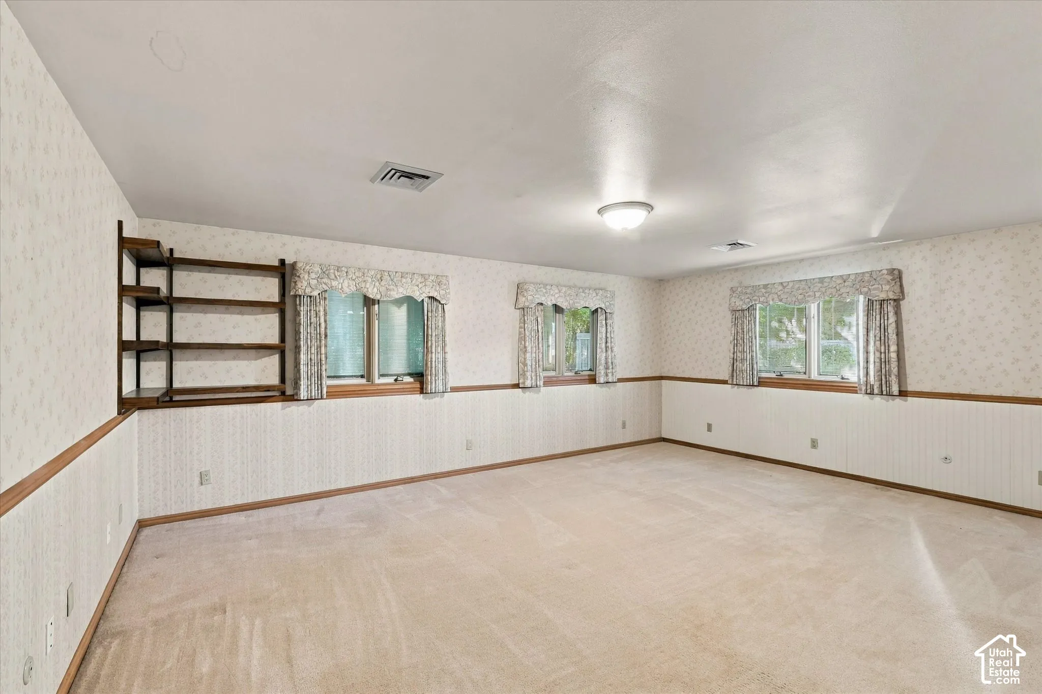 Spacious room featuring three windows, a built-in shelving unit, wall-to-wall carpeting, and a ceiling-mounted light fixture