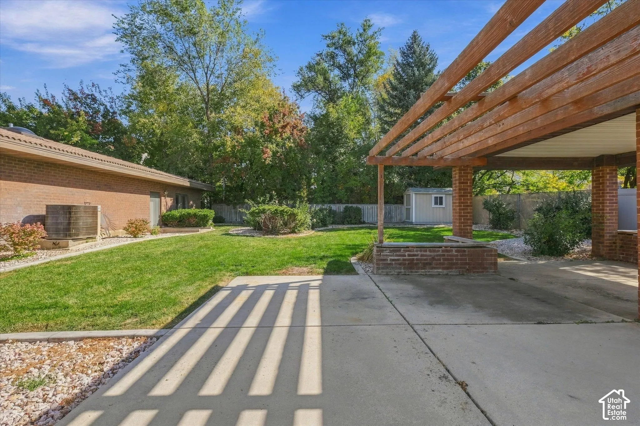 Expansive concrete patio with a wooden pergola, brick columns, and a manicured lawn