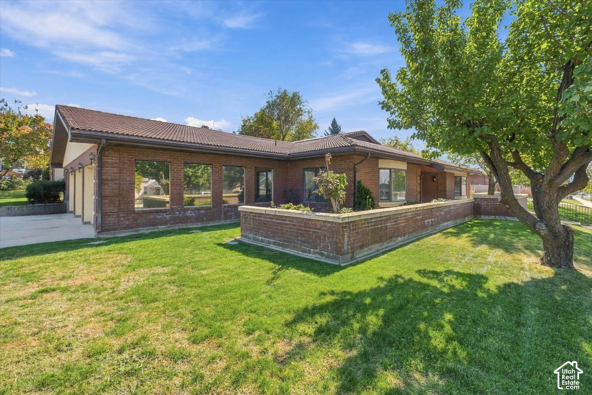 Brick exterior with a tiled roof, mature landscaping, and a three-car garage