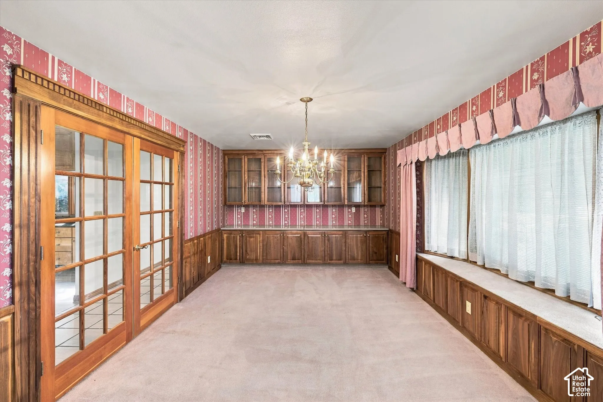 Room featuring French doors, a built-in window bench, custom cabinetry with glass-front uppers, and a brass chandelier