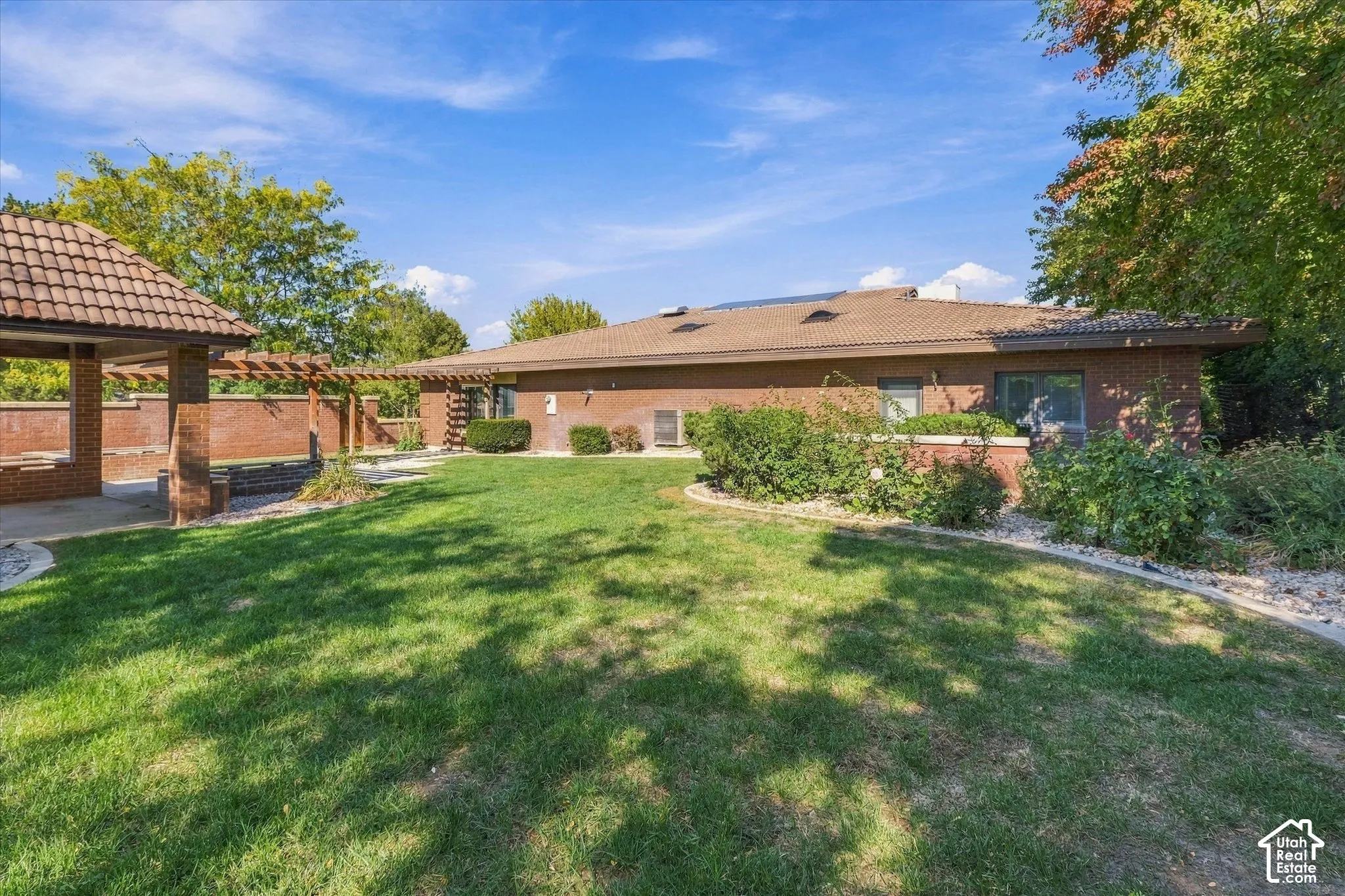 Expansive lawn area, brick exterior, tile roof, covered patio with tile roof, and a wooden pergola structure