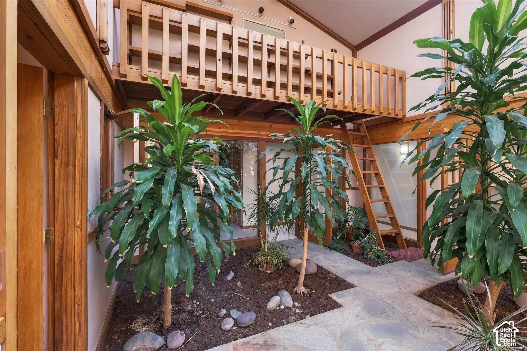 Interior courtyard with natural stone flooring, wood-framed windows, a wood-slat balcony, and a wood ladder