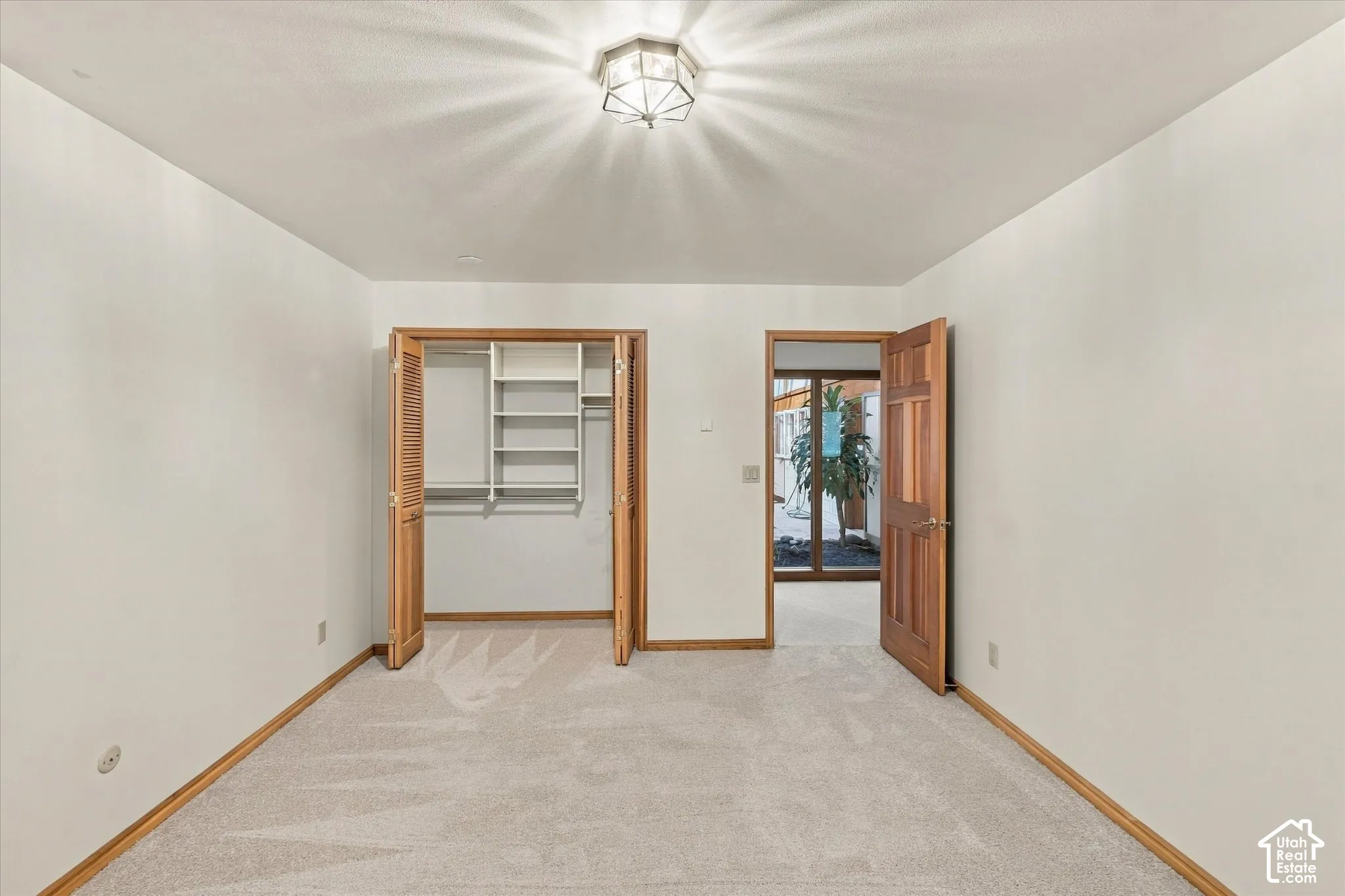 Spacious bedroom with warm wood-finish door frames, neutral carpeting, and abundant natural light