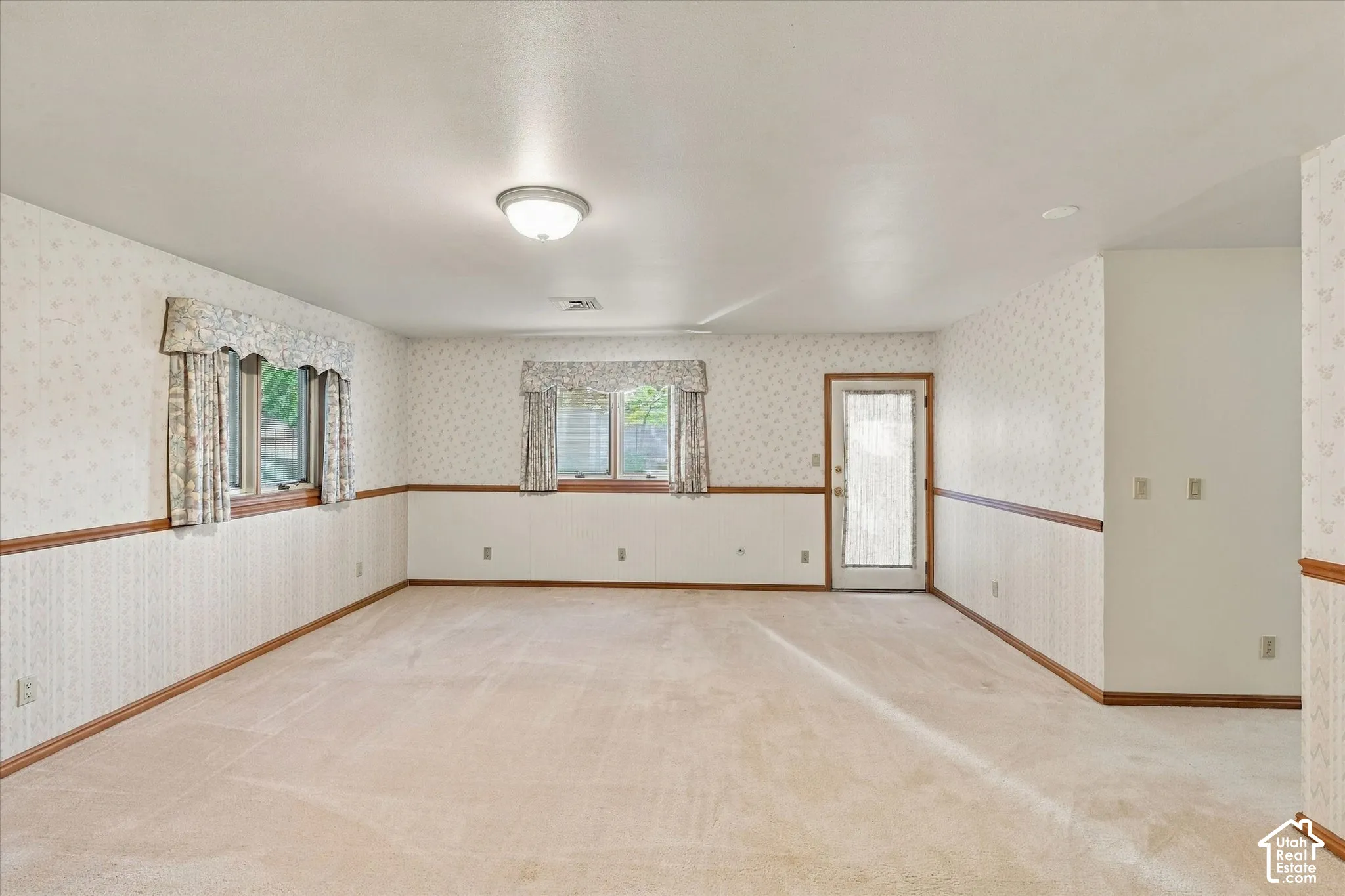 Carpeted room with wall paneling and two windows, featuring a ceiling-mounted light fixture and an exterior door with frosted glass
