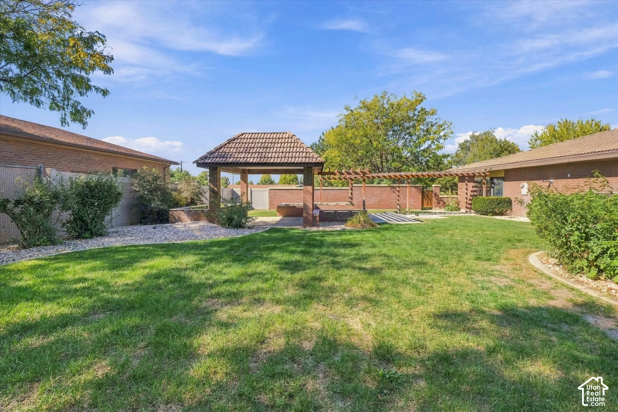 Expansive lawn featuring mature landscaping, a tiled-roof gazebo, brick perimeter wall, and a wood pergola structure