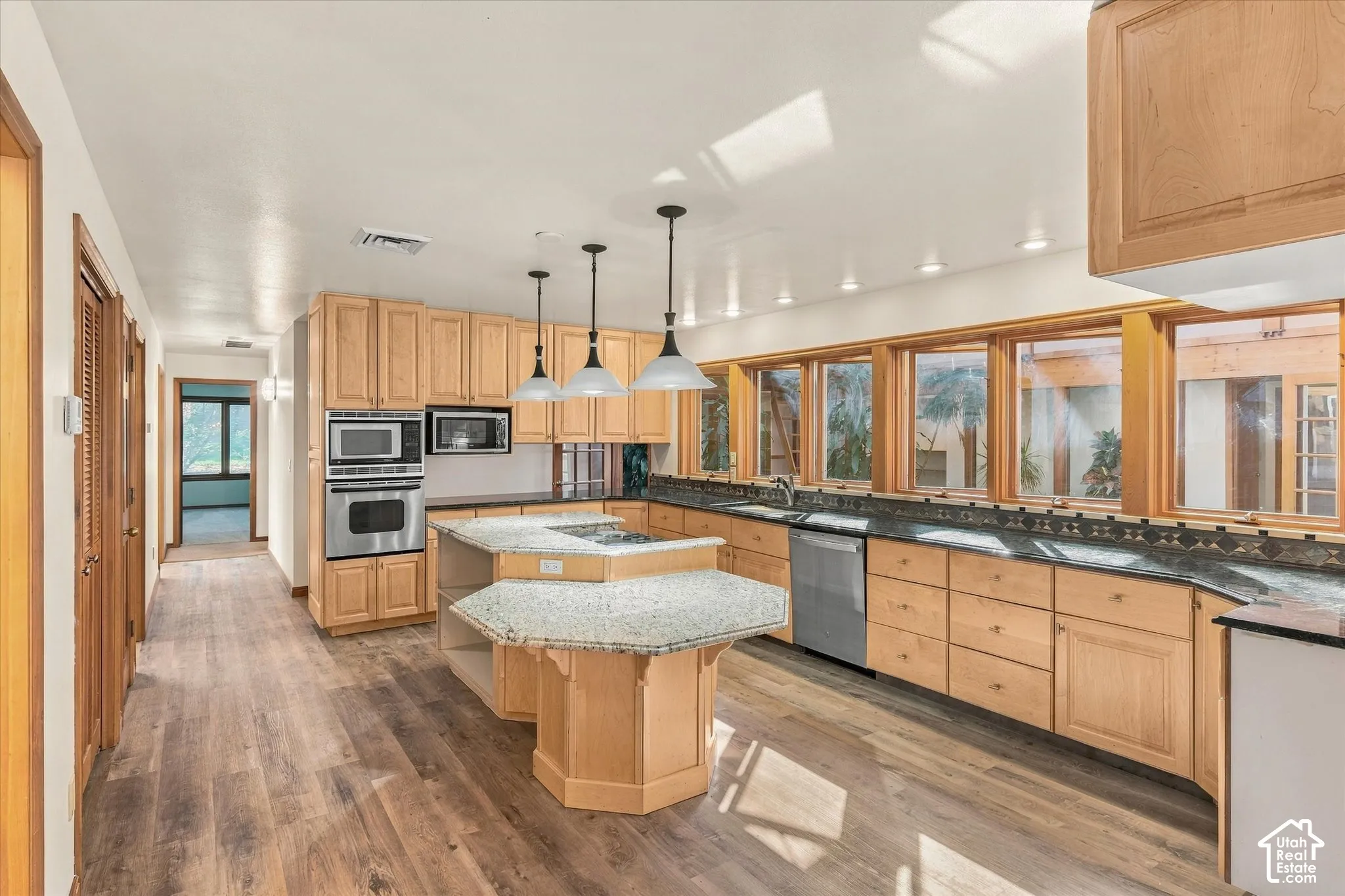 Kitchen featuring dual islands with stone countertops, stainless steel appliances, wood-finish flooring, ample cabinetry, and an expansive window line