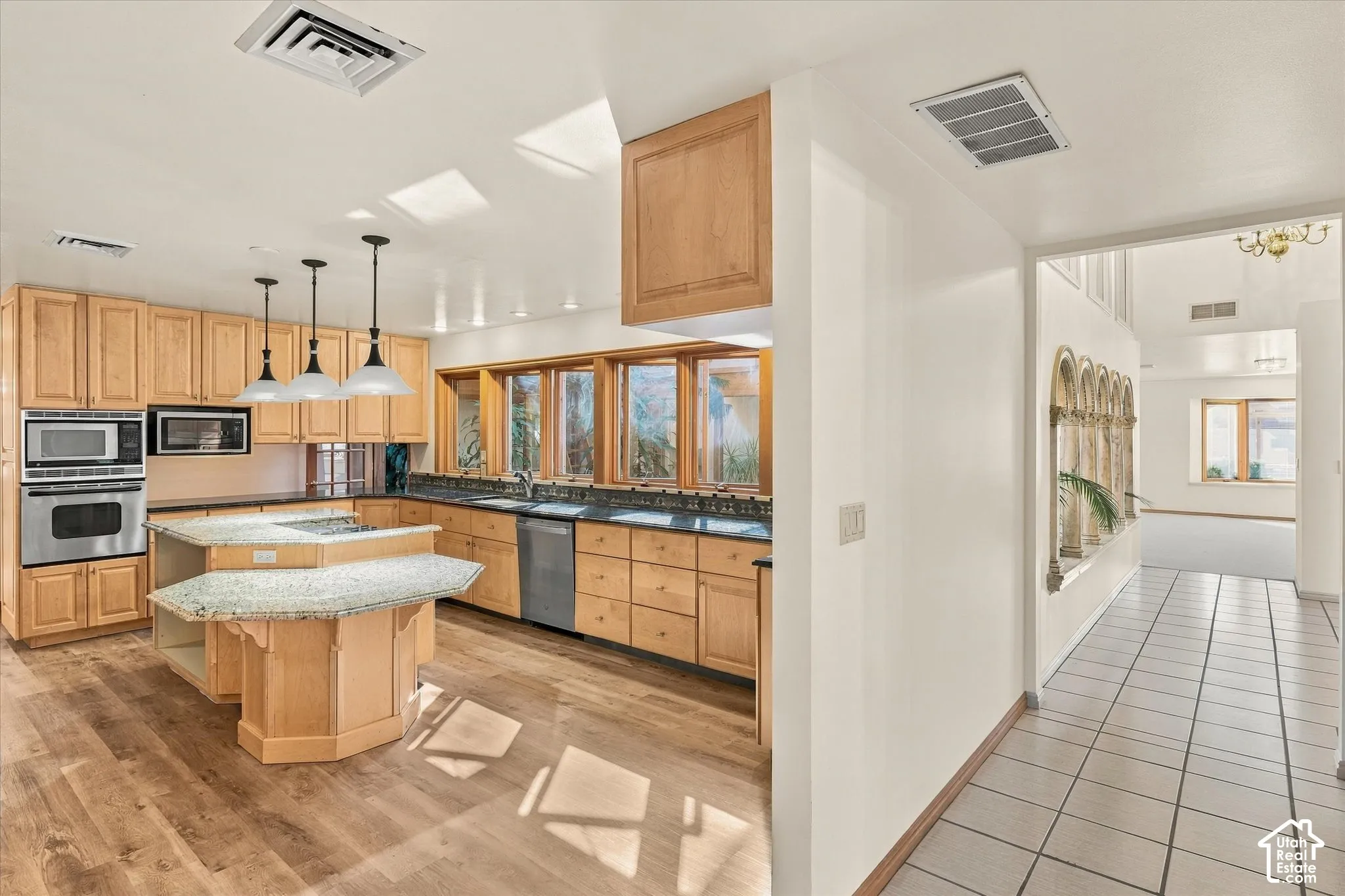 Open-concept kitchen featuring wood-finish flooring, light-toned cabinetry, stainless steel appliances, and a central island with a multi-level countertop