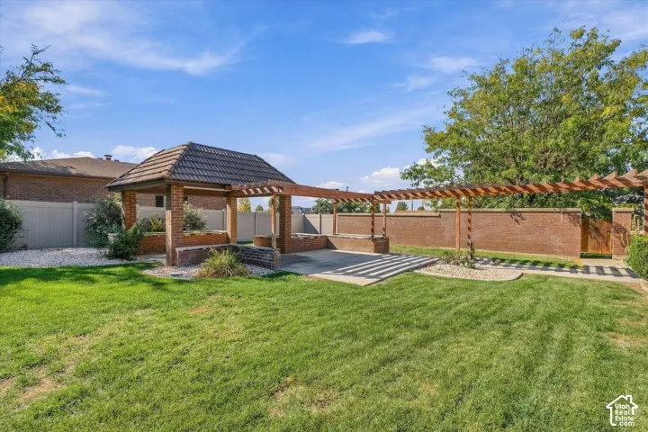 Expansive backyard featuring a brick gazebo with a tiled roof, an extended pergola, a concrete patio area, and a brick privacy wall