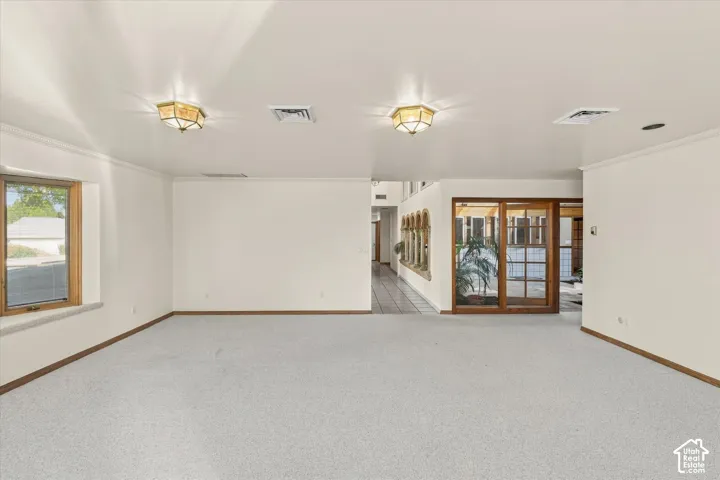 Expansive room featuring light-colored carpeting, white wall finishes, and crown molding