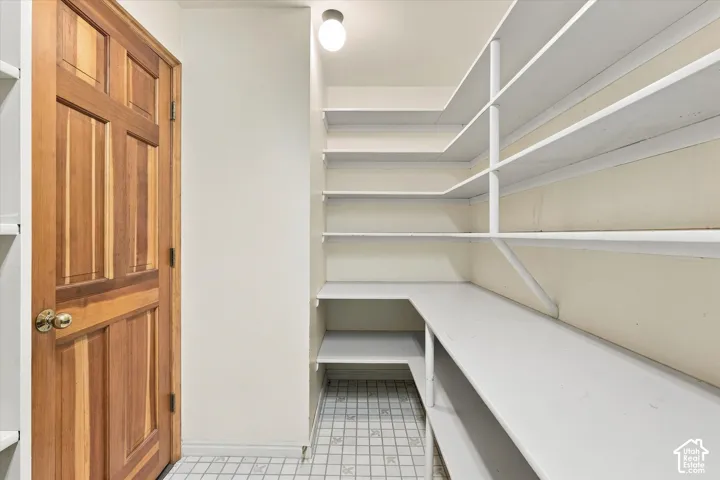 Large panty with extensive storage, wood-paneled door and tiled flooring.