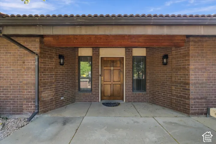 Brick exterior featuring a wooden entry door, sidelight windows, overhead wood-finish beam, and exterior sconces
