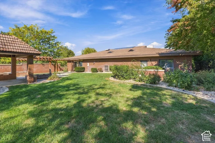 Expansive lawn area, brick exterior, tile roof, covered patio with tile roof, and a wooden pergola structure