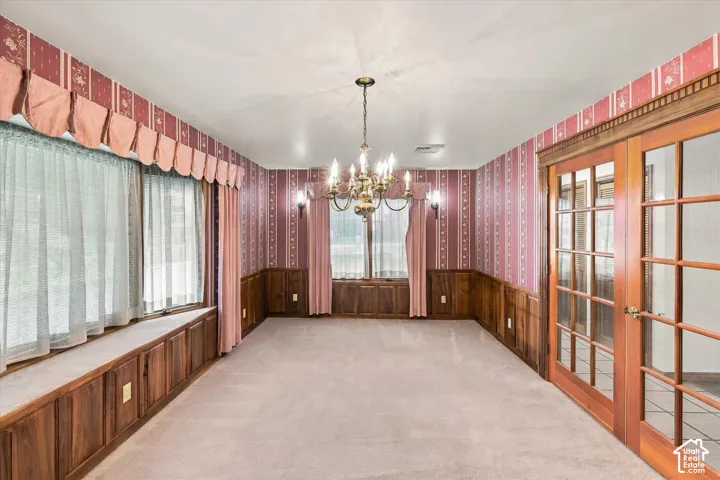 Carpeted flooring, wood paneling, wood-frame French doors, built-in window seating, and a chandelier with wall sconces