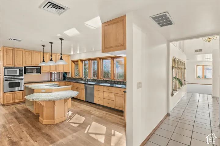 Open-concept kitchen featuring wood-finish flooring, light-toned cabinetry, stainless steel appliances, and a central island with a multi-level countertop