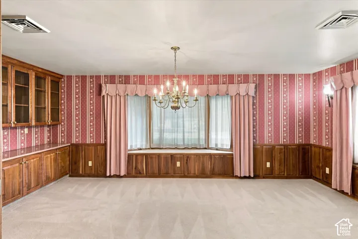 Built-in display cabinetry, wood paneling, a bay window with integrated storage, and a brass chandelier