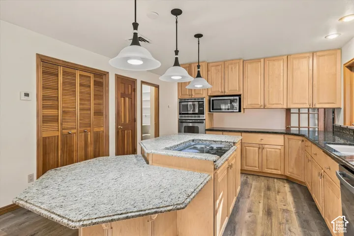 Kitchen featuring light wood cabinetry, a two-tiered island with light granite countertops, a built-in cooktop, and stainless steel appliances