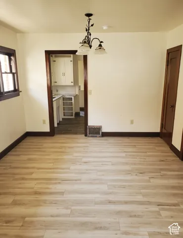 Light-toned wood-finish flooring, dark wood trim, and a decorative ceiling light fixture