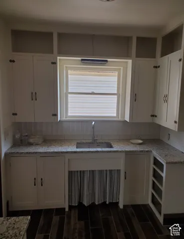 White cabinetry with open shelving, double basin sink, granite-style countertops, white subway tile backsplash, and wood-look flooring
