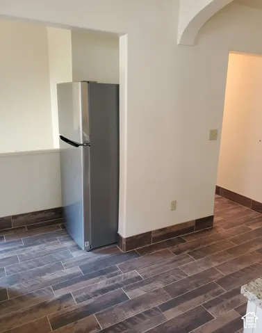 Stainless steel refrigerator, wood-finish tile flooring, recessed appliance nook, arched entryway, and neutral wall tones