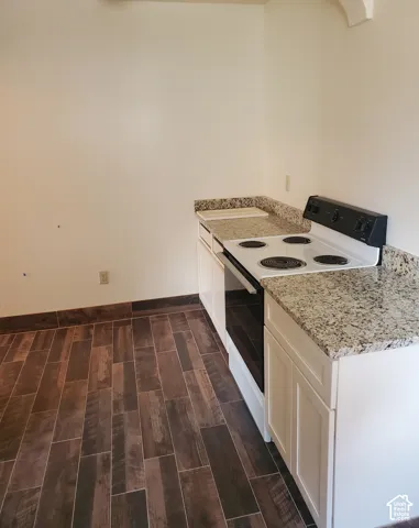 White cabinetry with shaker-style doors, speckled countertops, and wood-finish flooring