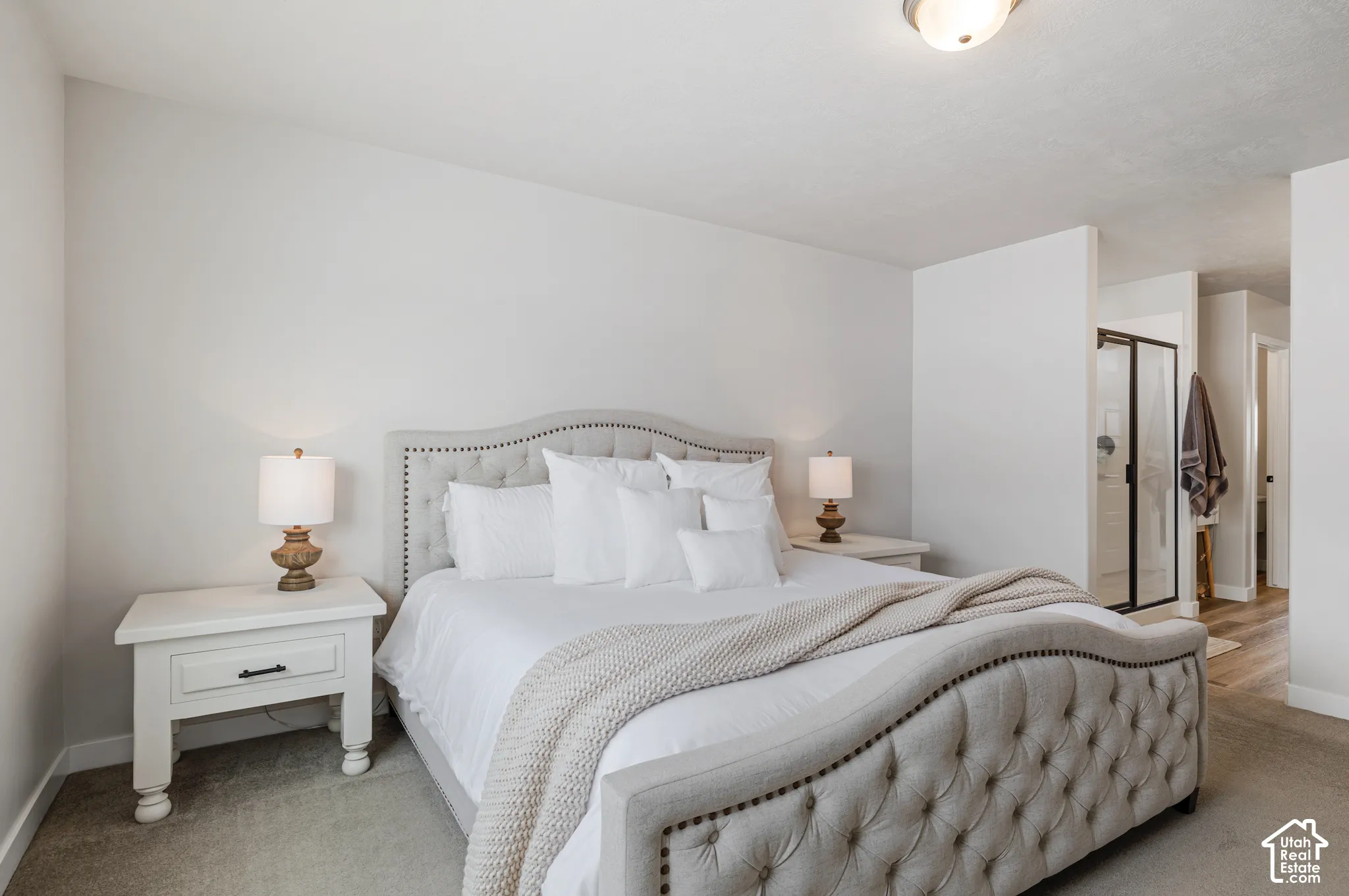 Carpet flooring, white walls, ceiling-mounted light fixture, white nightstands, and a glass-enclosed shower