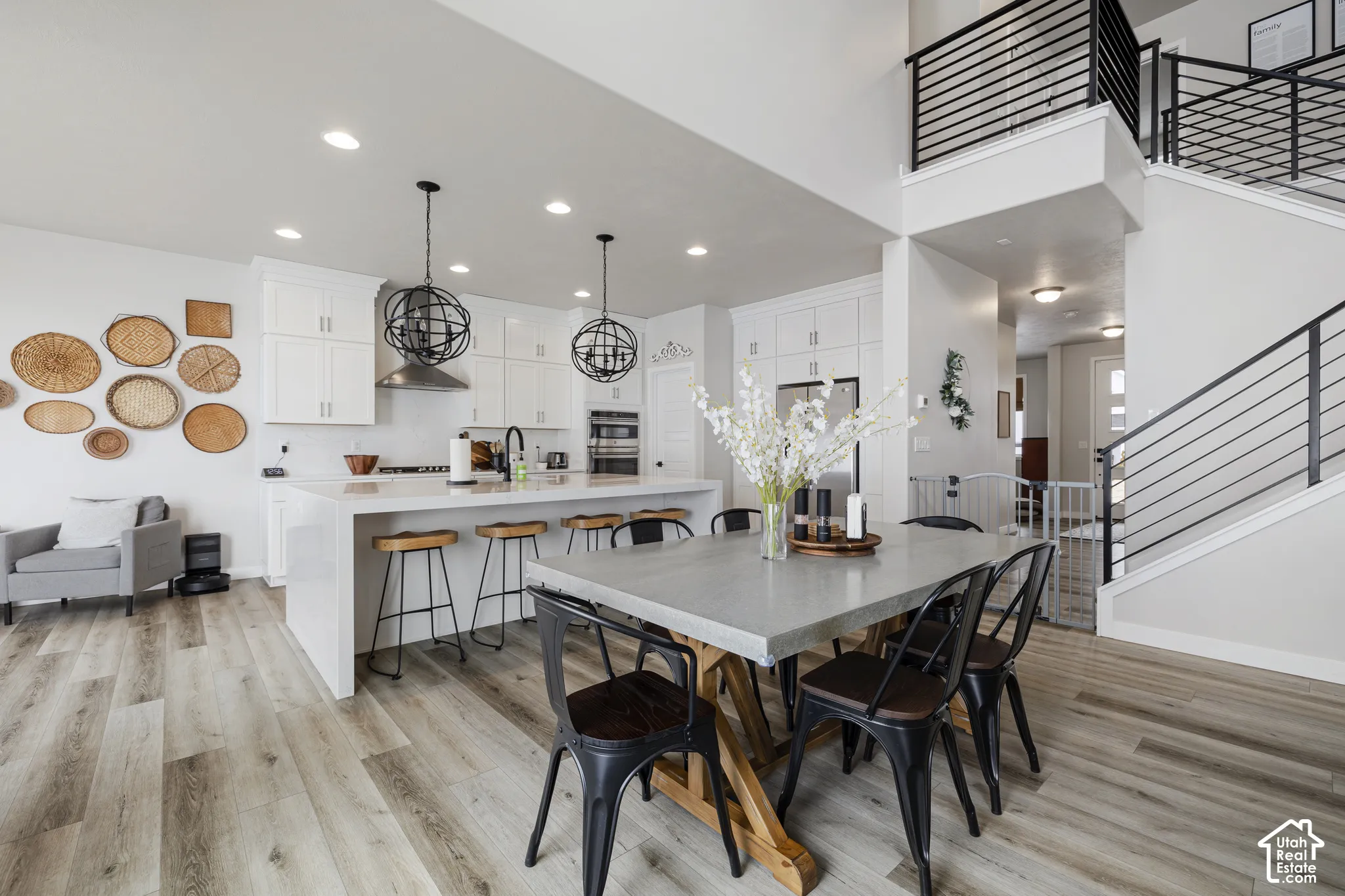 Open-concept living space featuring wood-finish flooring, a kitchen with white cabinetry and an island, a dining area, and a staircase with contemporary black metal railings