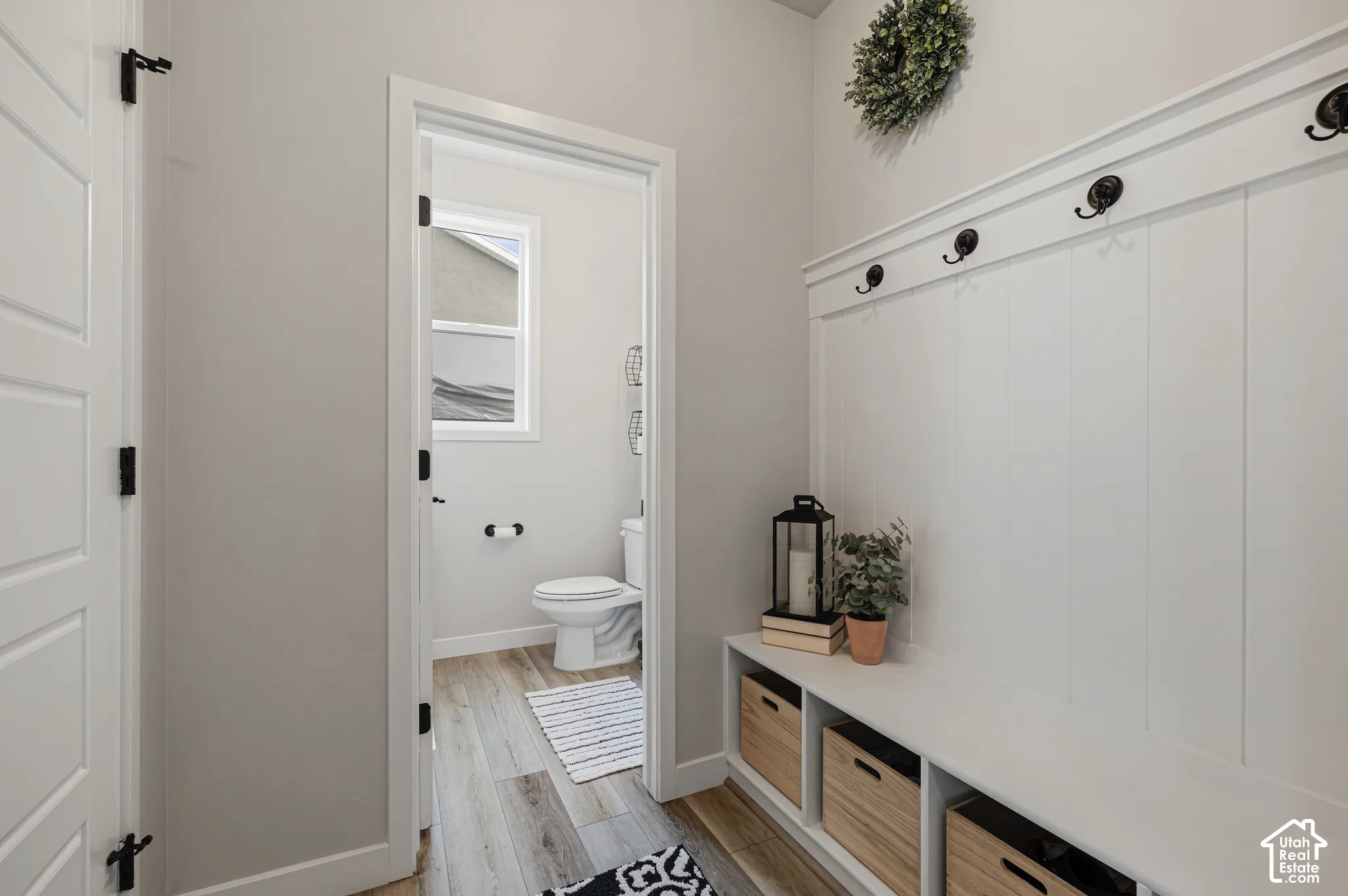 Built-in bench with storage cubbies and coat hooks, paneling, and wood-finish flooring