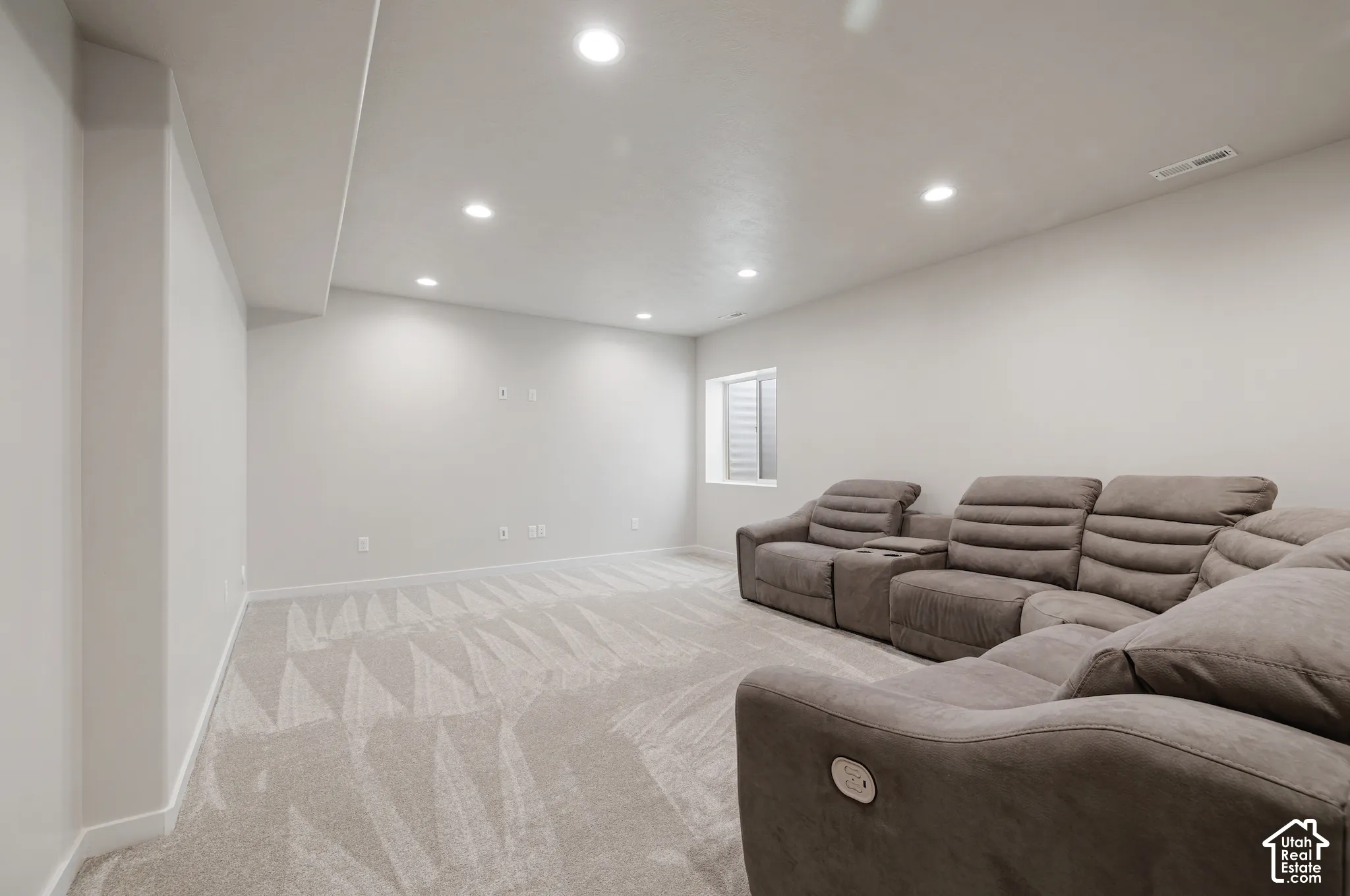 Recessed lighting illuminates an expansive room with light-colored walls and patterned carpeting