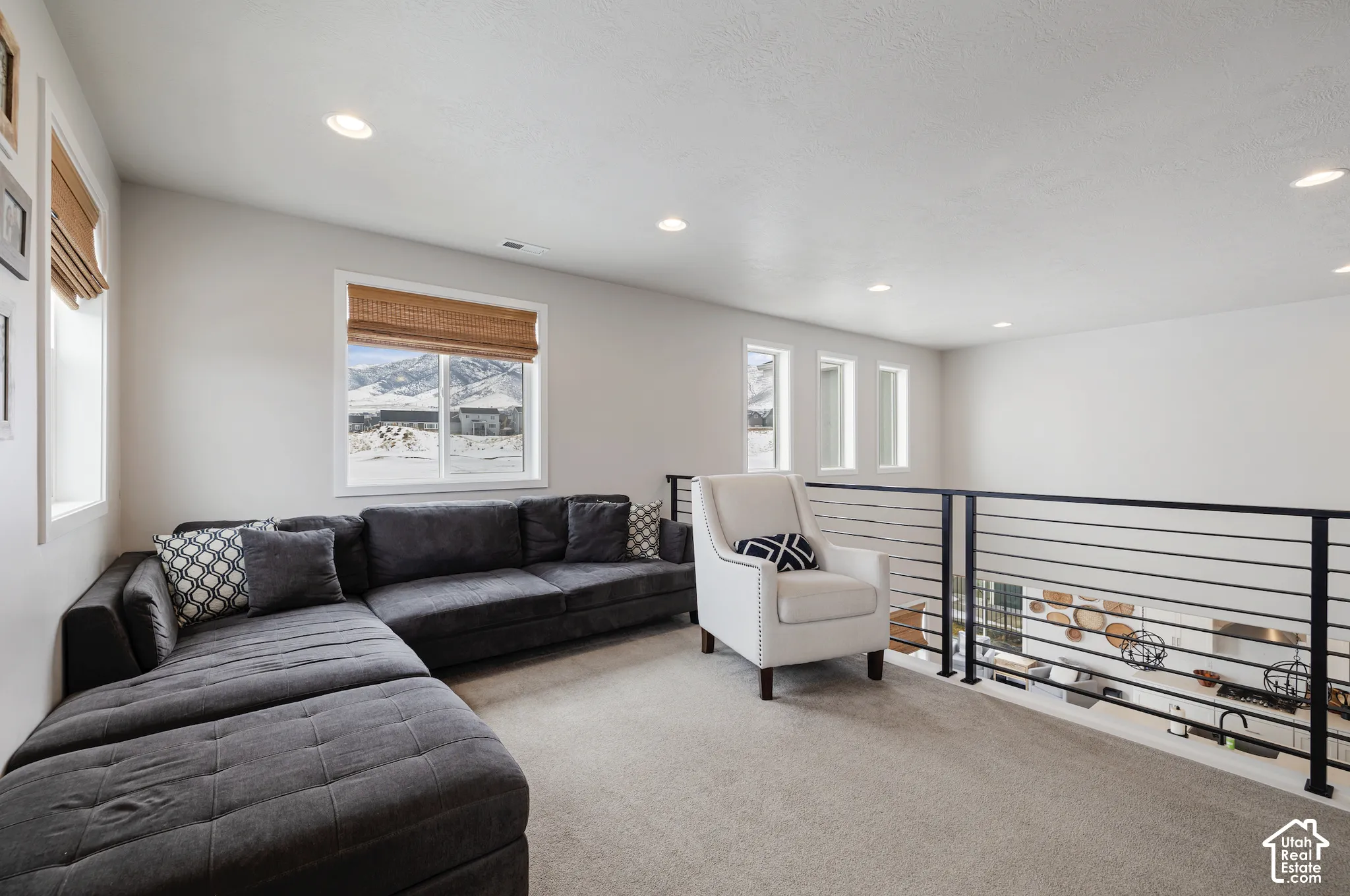 Recessed lighting illuminates the carpeted loft space with a black horizontal-bar railing overlooking a lower level