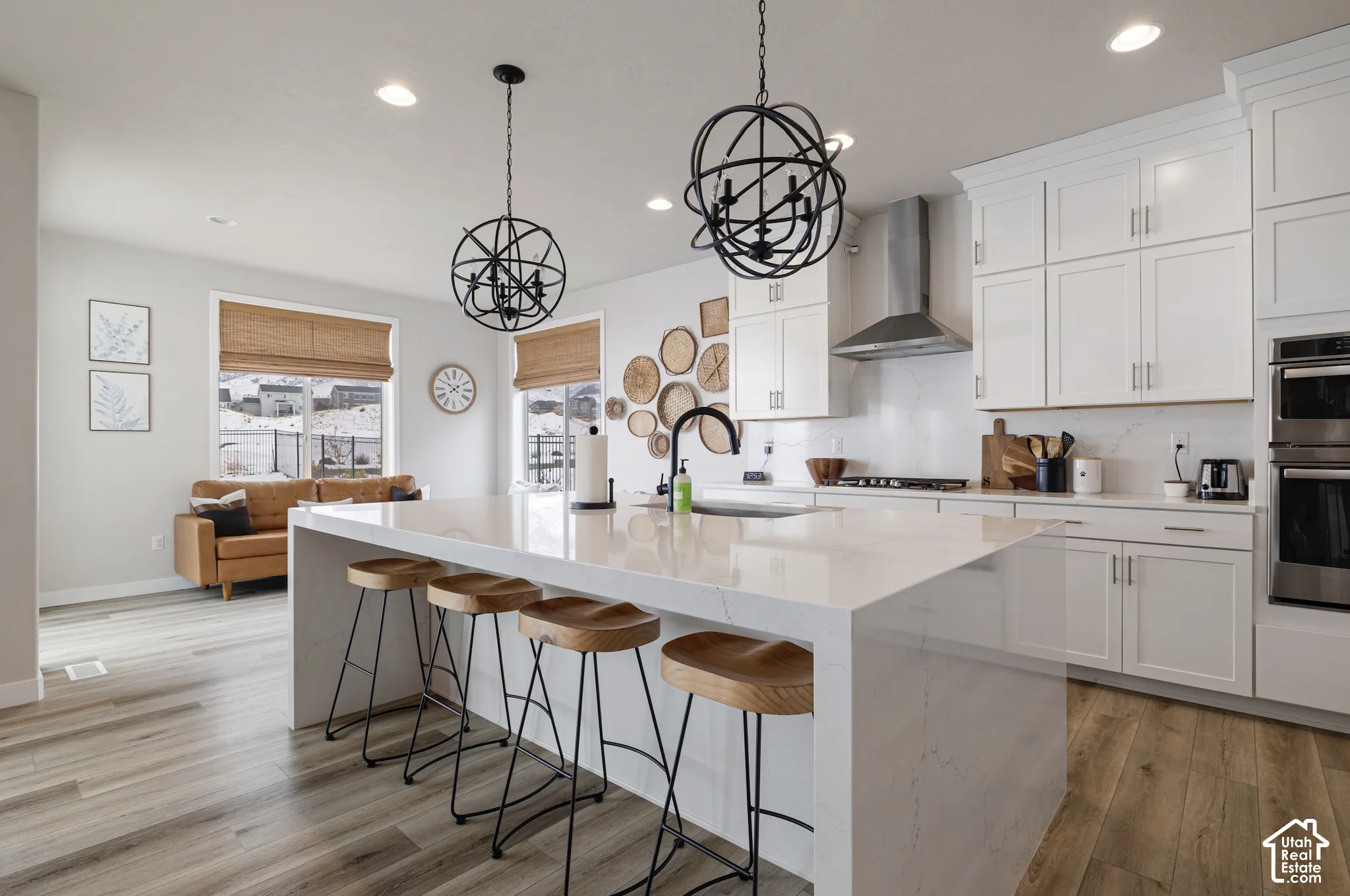 Spacious kitchen featuring white cabinetry, a large waterfall island with seating, a stainless steel range hood, and integrated double ovens