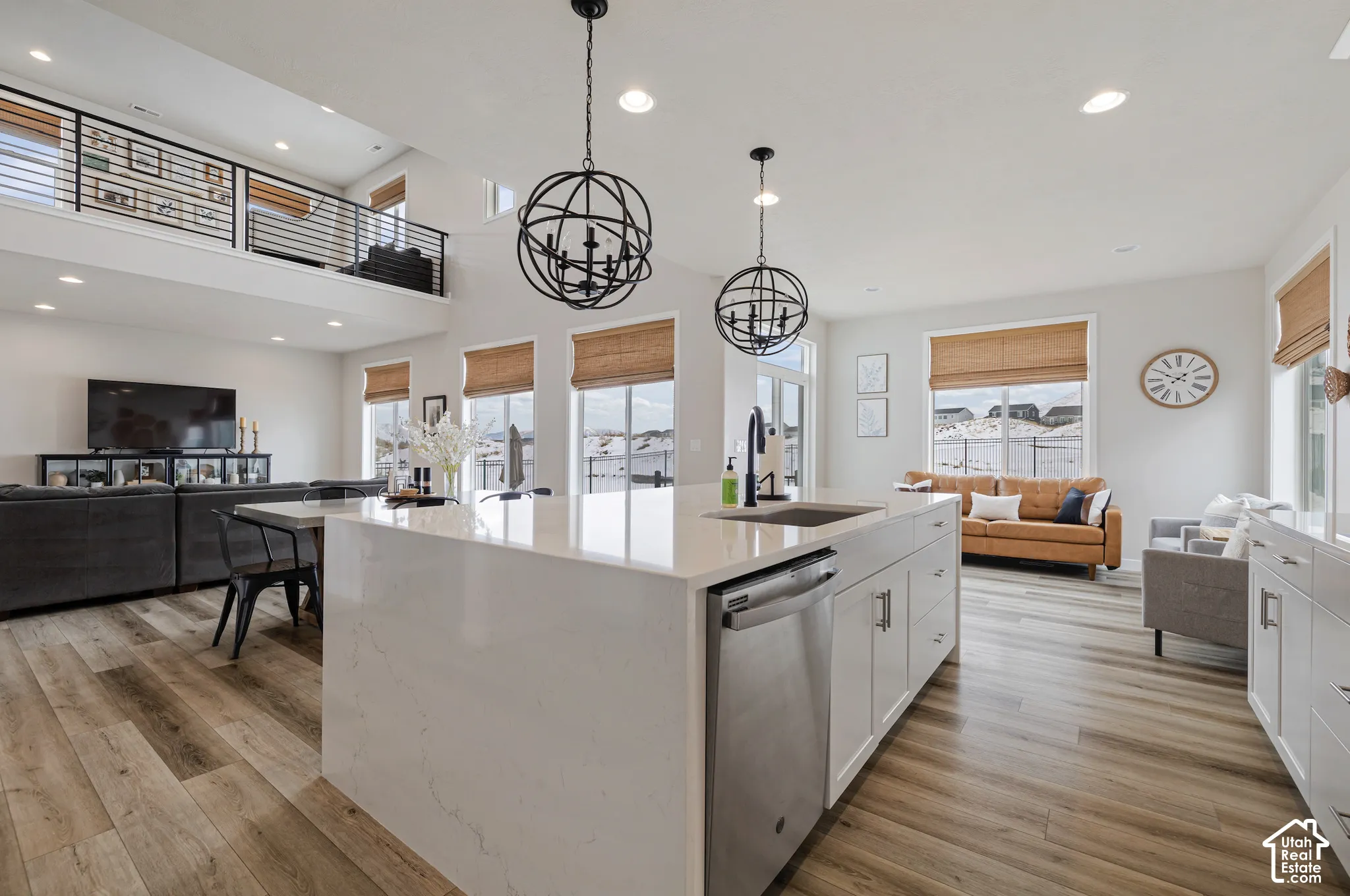 Open-concept living area with wood-finish flooring, a kitchen island with integrated sink, stainless steel appliances, and white cabinetry