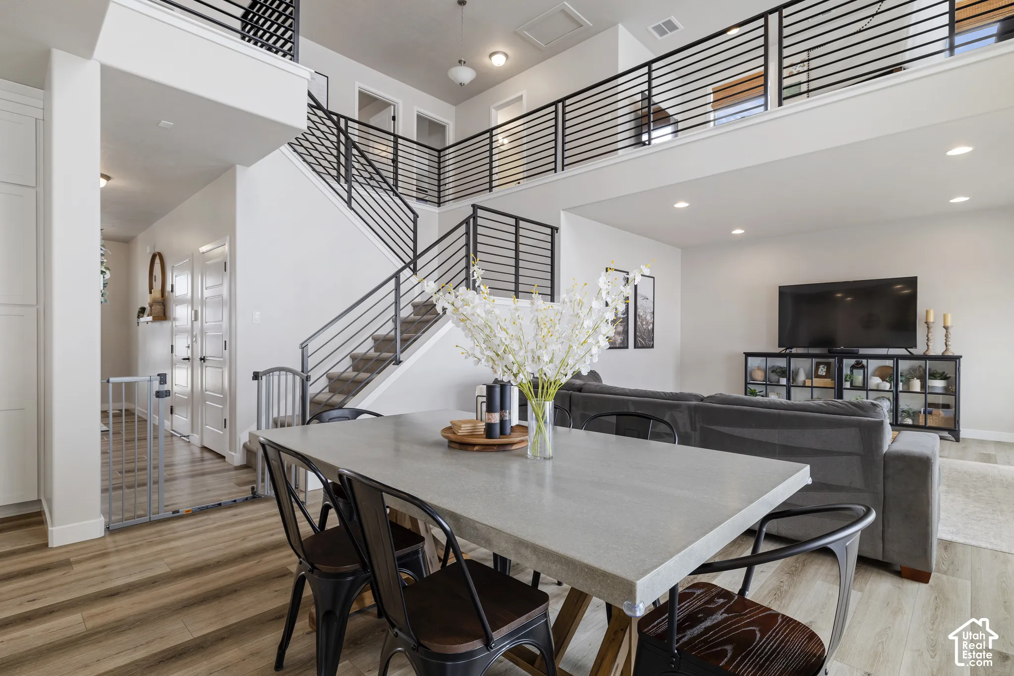 Open-concept living area featuring a two-story ceiling, wood-finish flooring, recessed lighting, and a contemporary staircase with metal railings