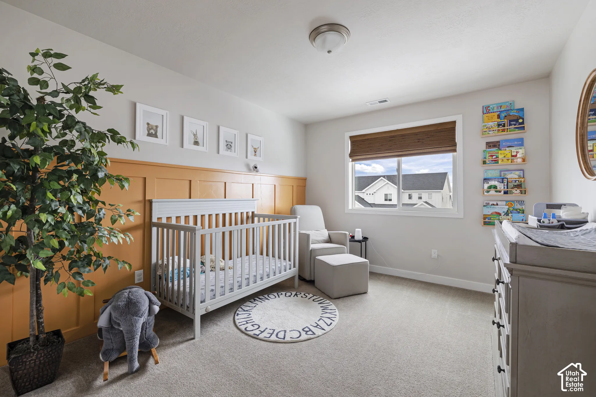 Carpeted room featuring a window with a woven shade, accent wall with paneling, and an overhead flush mount light fixture