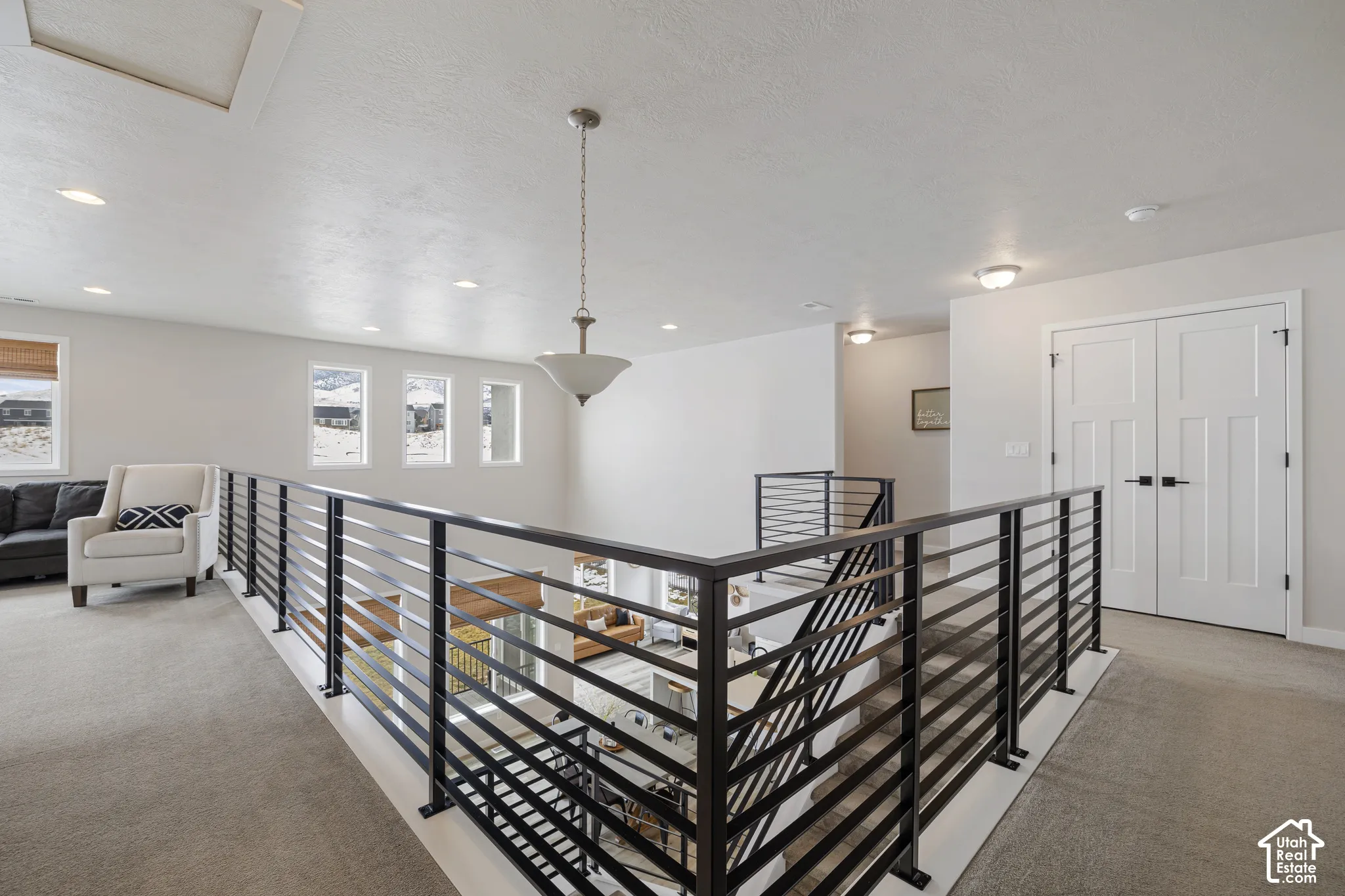 Open loft area featuring a modern horizontal metal railing, multiple windows, recessed ceiling lights, and a central pendant light fixture