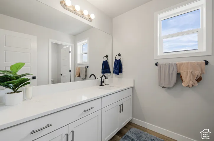 White shaker cabinetry with brushed nickel hardware, expansive vanity with white countertop, undermount sink with matte black faucet, wood-finish flooring, and a large mirror