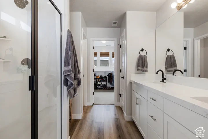 Double vanity with white cabinetry and integrated sinks, matte black fixtures, wood-finish flooring, and a walk-in shower with clear glass enclosure