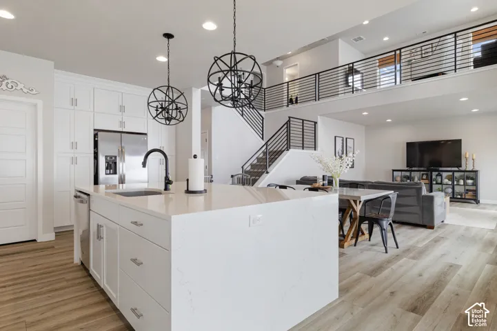 Gourmet kitchen featuring a large island with sink, white cabinetry, stainless steel appliances, and wood-finish flooring