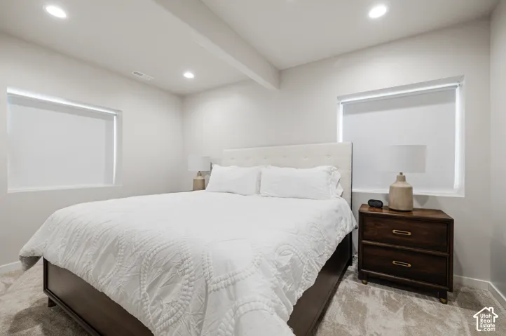 Recessed lighting illuminates this room, featuring carpeted flooring and dual windows with roller shades