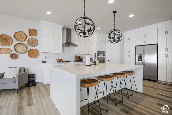 Spacious kitchen featuring white cabinetry, a large center island with seating, wood-finish flooring, stainless steel appliances, and orb chandeliers