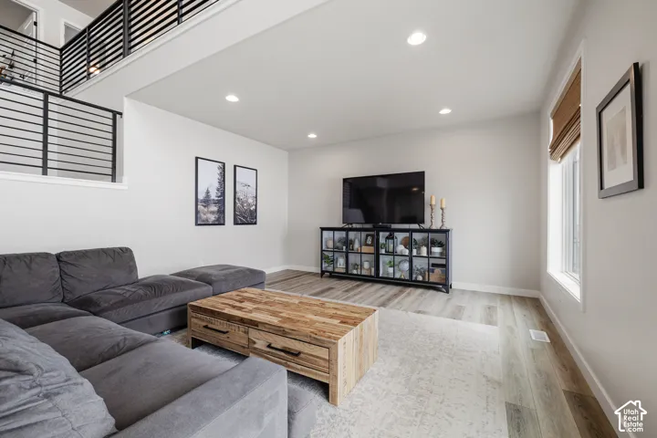 Spacious living area featuring wood-finish flooring, recessed lighting, a modern horizontal metal railing, and a window with a roller shade