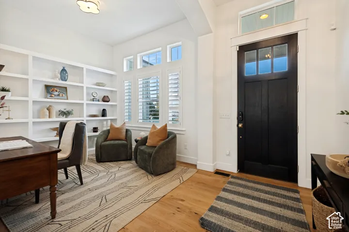 Entryway featuring a dark wood-finish door with glass panels, light wood-finish flooring, built-in shelving, white plantation shutters, and a transom window