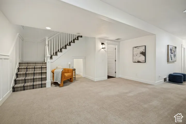 Plush carpeting throughout, a staircase with plaid carpet, white wainscoting, and recessed lighting