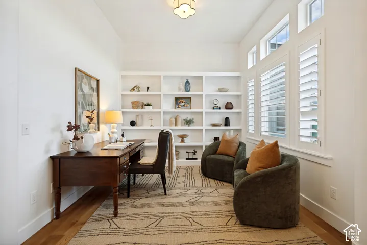 Wood-finish flooring with built-in shelving, complemented by multiple windows with white plantation shutters, and a decorative ceiling light fixture